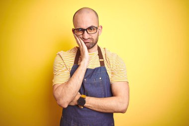 Barista önlük giyen genç barmen adam sarı arka plan üzerinde profesyonel olarak çalışan yorgun görünümlü ve çapraz kolları ile depresyon sorunları ile sıkılmış düşünme.