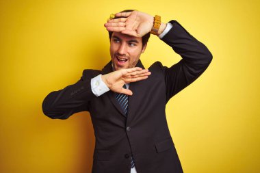 Takım elbise ve kravat giyen genç yakışıklı işadamı izole sarı arka plan üzerinde duran Gülümseyen neşeli oynarken elleri yüzünü gösteren bir boo gözetleme. Şaşırttı ve çıktı