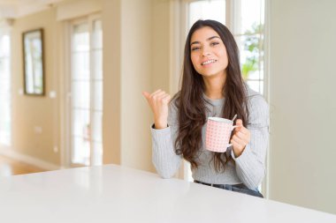 Genç kadın bir fincan kahve içerken işaret eden ve başparmak ile gösteren mutlu yüzü gülümseyerek yan