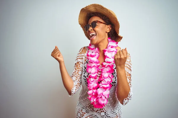 Young african american woman with afro hair wearing flower hawaiian lei over isolated background very happy and excited doing winner gesture with arms raised, smiling and screaming for success. Celebration concept.