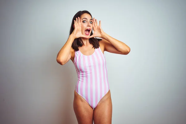 年轻美丽的女人穿着条纹粉红色泳装泳装在孤立的背景微笑欢快玩偷看一个嘘声与双手显示的脸 惊讶和退出 — 图库照片