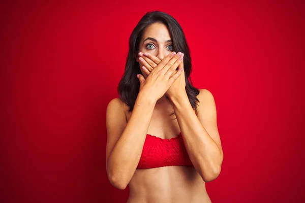 穿着比基尼泳装的美丽女人在红色孤立的背景震惊覆盖嘴与手的错误 秘密概念 — 图库照片