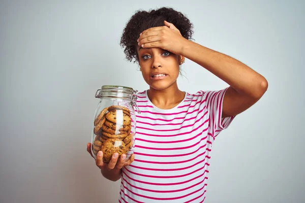 Young african american woman holding a jar of cookies over isolated white background stressed with hand on head, shocked with shame and surprise face, angry and frustrated. Fear and upset for mistake.