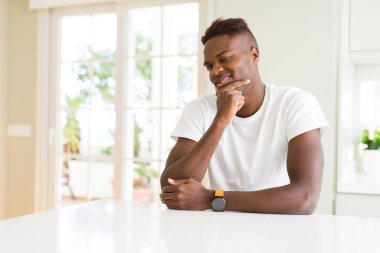 Yakışıklı afro-amerikan adam evde beyaz masada çapraz kolları ve çene üzerinde kaldırdı ile gülümseme ile kameraya emin bakıyor. Olumlu düşünme.