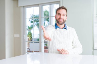 Yakışıklı adam rahat kazak giyen tebrik ve karşılama olarak el sıkışma sunan dostu gülümseyerek. Başarılı iş.