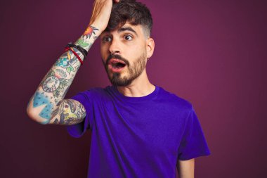 Dövmeli genç adam izole mor arka plan üzerinde duran t-shirt giyen hata için kafasına el ile şaşırttı, hata hatırlıyorum. Unuttum, kötü bellek kavramı.
