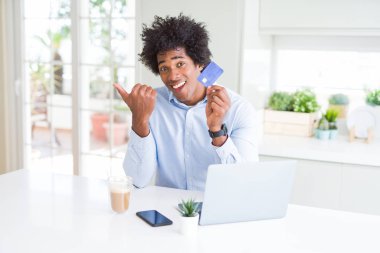 Afro-Amerikan adam dizüstü bilgisayar ve kredi kartı ile online alışveriş kullanarak işaret ve mutlu yüzü gülümseyerek yan başparmak ile gösteren