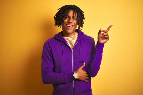 非洲裔美国男子穿着紫色运动衫 在孤立的紫色背景上 脸上挂着灿烂的笑容 用手和手指指着一边看着相机 — 图库照片