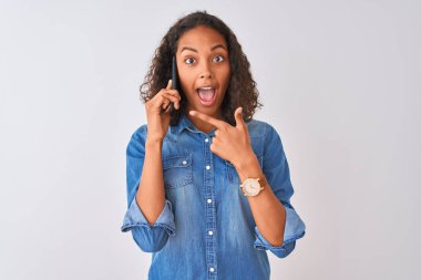 Genç Brezilyalı kadın izole beyaz arka plan üzerinde duran akıllı telefon üzerinde konuşurken çok mutlu el ve parmak ile işaret