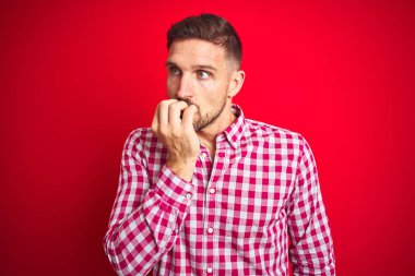 Kırmızı izole arka plan üzerinde genç yakışıklı adam stresli ve ağız tırnak ısırma elleri ile sinir görünümlü. Anksiyete sorunu.