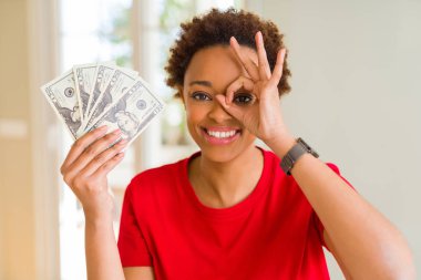 Genç afro-amerikan kadın mutlu yüz ile yirmi dolar banka banknotları tutan parmakları ile bakarak göz eliyle ok işareti yapıyor gülümseyerek