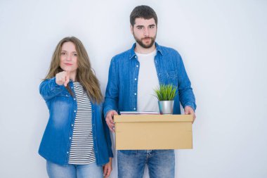 Beyaz izole arka plan üzerinde yeni eve hareket karton kutu tutan genç çift kameraya parmak ile işaret ve size, el işareti, önden olumlu ve kendinden emin jest