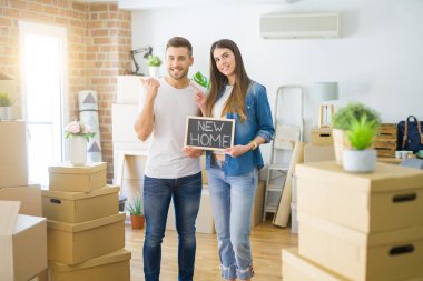 Genç güzel çift yeni evde yeni ev metni ile tahta tutan işaret ve mutlu yüz gülümseyerek yan başparmak ile gösteren