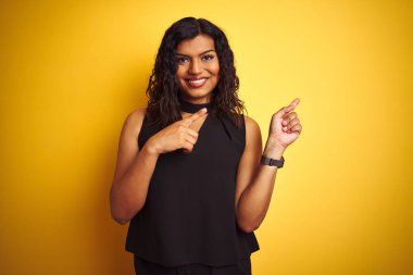 Transseksüel transseksüel zarif iş kadını izole sarı arka plan üzerinde gülümseyerek ayakta ve yan iki el ve parmak ile işaret kamera bakarak.