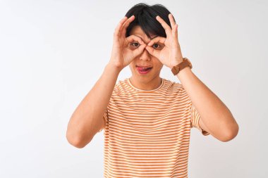 Izole beyaz arka plan üzerinde duran rahat çizgili t-shirt giyen genç Çinli adam dürbün dil dışarı yapışmasını gibi ok jest yapıyor, gözleri parmaklardan bakıyor. Çılgın ifade.