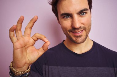 Genç yakışıklı adam parmakları, mükemmel sembolü ile ok işareti yapıyor izole pembe arka plan üzerinde duran rahat t-shirt giyiyor