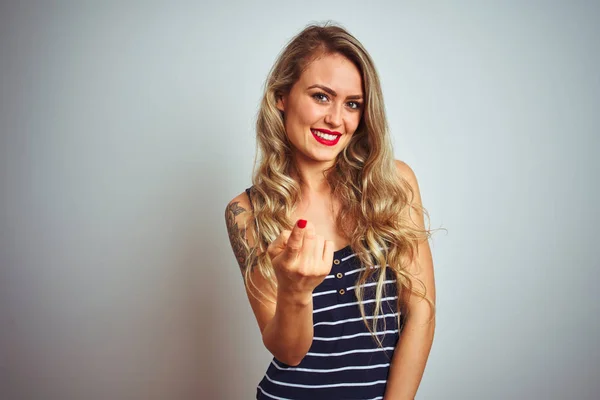 Young beautiful woman wearing stripes t-shirt standing over white isolated background Beckoning come here gesture with hand inviting welcoming happy and smiling