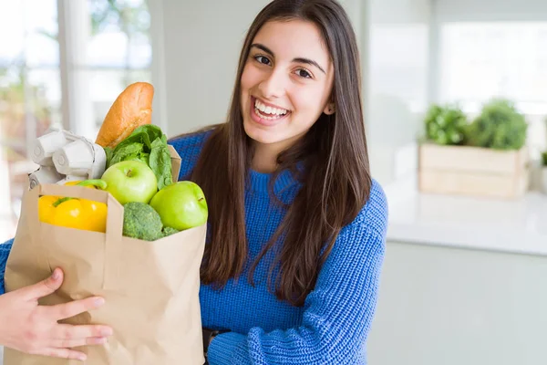 Jonge mooie vrouw glimlachend het houden van een papieren zak vol kruidenier — Stockfoto