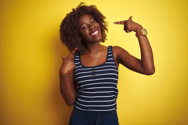 Young african afro woman wearing striped t-shirt over isolated yellow background smiling cheerful showing and pointing with fingers teeth and mouth. Dental health concept.