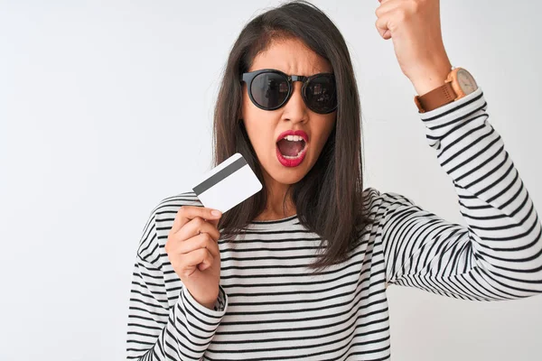 Young chinese woman wearing sunglasses holding credit card over isolated white background annoyed and frustrated shouting with anger, crazy and yelling with raised hand, anger concept