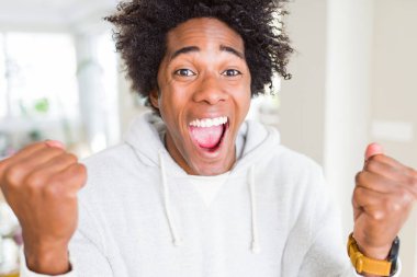 Afrika kökenli Amerikalı adam silah ile başarı için heyecanlı kazak giyen zafer kutluyor gülümseyen kaldırdı. Kazanan kavramı.