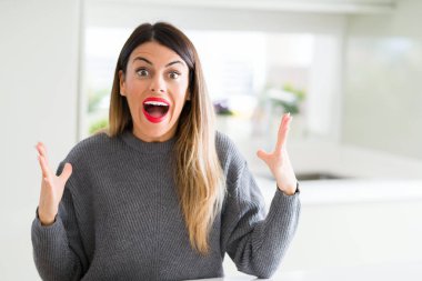 Evde kış kazak giyen genç güzel kadın deli ve başarı için hayran kaldırdı kollarını açarak kutluyor ve heyecanlı çığlık gözleri açık. Kazanan kavramı