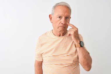 Üst düzey gri saçlı adam çizgili t-shirt izole beyaz arka plan üzerinde duran giyen göz jest, şüpheli ifade izlerken