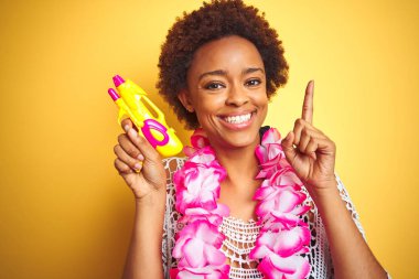 Afro saçlı genç afro-amerikalı kadın çiçek hawaiian lei ve su tabancası giyen mutlu yüz, bir numaralı ile bir fikir ya da soru işaret parmak ile şaşırttı