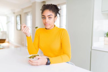 Genç afro-amerikan kadın sağlıklı yeşil vegatables yeme akıllı yüz ciddi düşünme kendine güvenen bir ifade ile