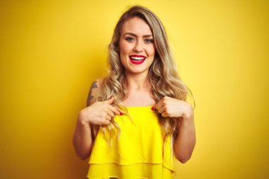 Genç attactive kadın sarı izole arka plan üzerinde duran t-shirt giyen yüzünde gülümseme ile emin görünümlü, parmakları gururlu ve mutlu kendini işaret.