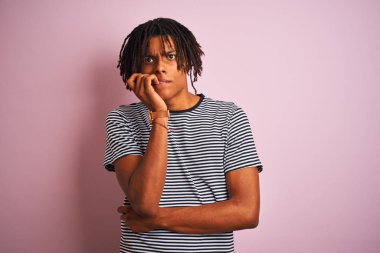Dreadlocks lacivert çizgili t-shirt izole pembe arka plan üzerinde duran giyen Afro adam stresli ve ağız tırnak ısırma elleri ile sinir görünümlü. Anksiyete sorunu.
