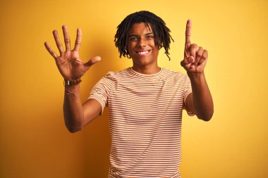 Çizgili t-shirt giyen dreadlocks giyen Afro adam izole sarı arka plan üzerinde duran gösteren ve emin ve mutlu gülümserken parmakları sayısı altı ile işaret.