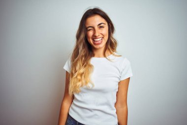 Genç güzel kadın izole arka plan üzerinde rahat beyaz t-shirt giyen seksi ifade, neşeli ve mutlu yüz ile kameraya bakarak göz kırpma.