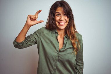 Gri izole arka plan üzerinde duran yeşil gömlek giyen genç güzel kadın gülümseyerek ve emin el parmakları görünümlü ve kamera ile küçük boyutlu işareti yapıyor gesturing. Ölçü kavramı.