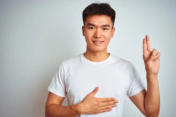 年轻的亚洲中国男子穿着T恤站在孤立的白色背景微笑发誓手在胸部和手指向上 作出忠诚的承诺誓言 — 图库照片