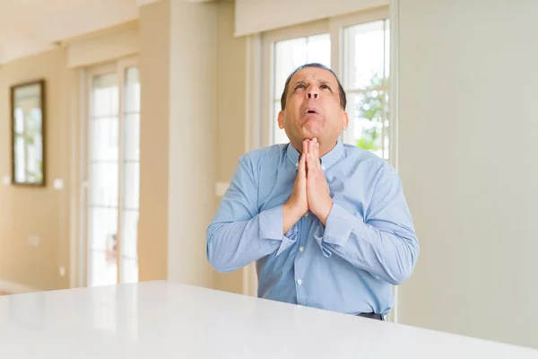 Homem Meia Idade Sentado Casa Implorando Orando Com Mãos Junto — Fotografia de Stock