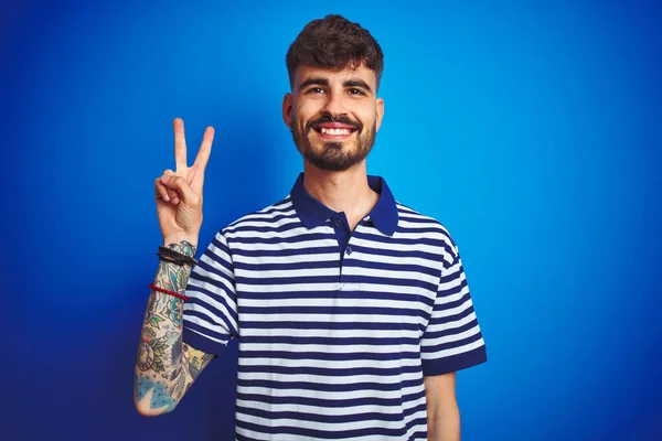 Mladý Muž Tetováním Proužkované Pólo Stojící Nad Izolovaným Modrým Pozadím — Stock fotografie
