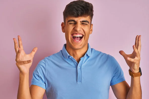 年轻的印度男子穿着蓝色马球站在孤立的粉红色背景庆祝疯狂和疯狂的成功与手臂抬起和闭上眼睛尖叫兴奋 优胜者概念 — 图库照片