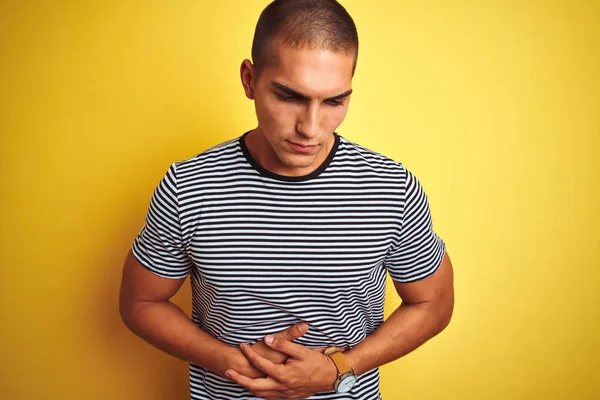 Genç yakışıklı adam mide üzerinde el ile sarı izole arka plan üzerinde çizgili t-shirt giyiyor çünkü hazımsızlık, ağrılı hastalık kötü hissediyorum. Ağrı kavramı.