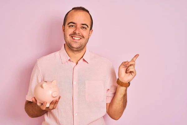 Junger Mann Hält Sparschwein Vor Isoliertem Rosa Hintergrund Und Zeigt — Stockfoto