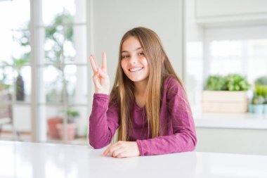 Beyaz masa üzerinde güzel genç kız çocuk gösteren ve parmakları ile işaret ederken üç numara kendinden emin ve mutlu gülümseyerek.