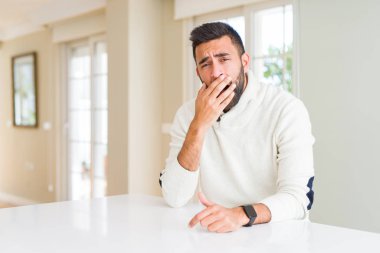 Yakışıklı İspanyol adam evde rahat beyaz kazak giyen el ile ağız kapsayan yorgun esneme sıkılmış. Huzursuz ve uykululuk.