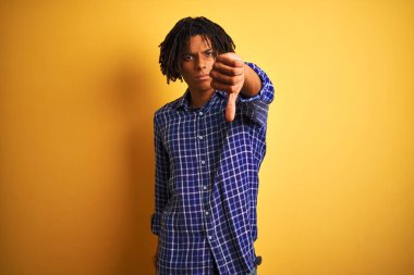 Yalnız sarı arka plan üzerinde duran rahat gömlek giyen dreadlocks ile Afro adam mutsuz ve kızgın gösteren reddi gösteren ve aşağı jest başparmak ile negatif. Kötü ifade.