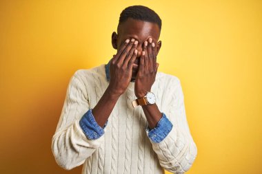 Izole sarı arka plan üzerinde denim gömlek ve beyaz kazak giyen Afro-Amerikan adam yorgunluk ve baş ağrısı, uykulu ve yorgun ifade için gözleri sürtünme. Görme sorunu