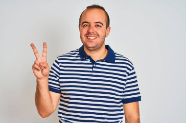 Yalnız beyaz arka plan üzerinde duran rahat çizgili polo giyen genç adam gösteren ve emin ve mutlu gülümserken parmakları ile iki işaret.