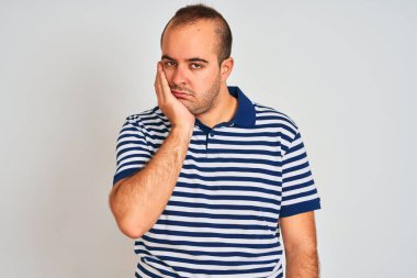 Izole beyaz arka plan üzerinde duran rahat çizgili polo giyen genç adam yorgun görünümlü ve çapraz kolları ile depresyon sorunları ile sıkılmış düşünme.