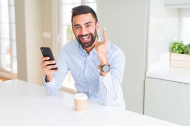 Yakışıklı İspanyol iş adamı kahve içme ve akıllı telefon kullanarak mutlu yüz, bir numaralı ile bir fikir veya soru işaret parmağı ile şaşırttı