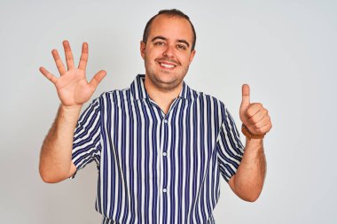 Mavi çizgili gömlek giyen genç adam izole beyaz arka plan üzerinde duran gösteren ve parmakları ile işaret ederken kendinden emin ve mutlu gülümseyerek altı numara.
