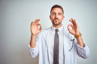 Genç yakışıklı doktor adam izole arka plan üzerinde beyaz profressional ceket giyen dinlenmek ve gözleri parmakları ile meditasyon jest yapıyor kapalı gülümseyerek. Yoga konsepti.