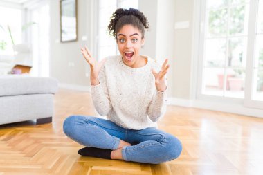 Afro saç ile güzel genç Afrikalı Amerikan kadın yerde oturan çılgın kutluyor ve başarı için hayran silah ile yükseltilmiş ve açık gözleri heyecanlı çığlık. Kazanan kavramı